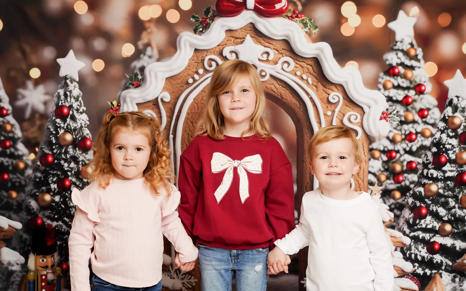 Three siblings holding hands beneath the Gingerbread Lane archway