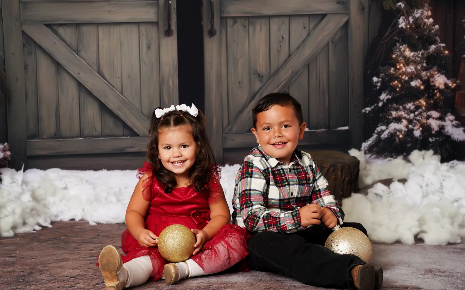 Two siblings holding gold ornaments in the snow at the Cozy Christmas Barn