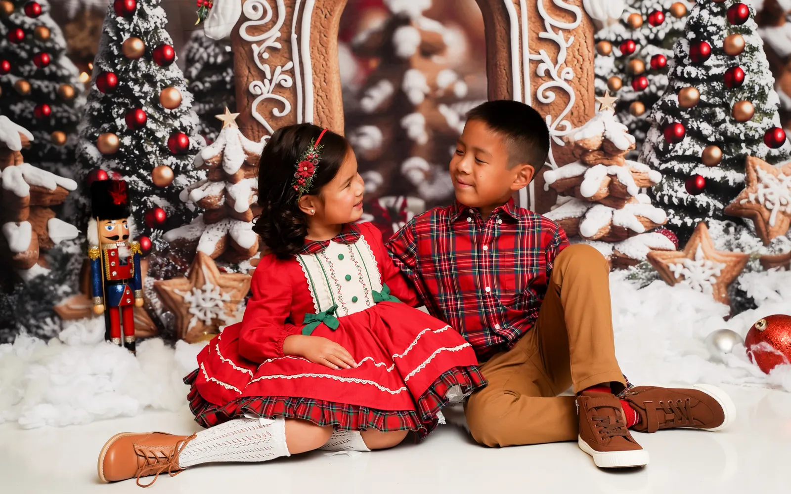 A brother and sister in red plaid smiling at each other on the Gingerbread Lane set