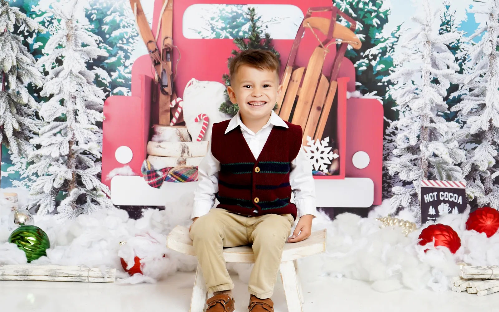 A boy in a plaid vest sitting on a stool in front of the Little Red Truck