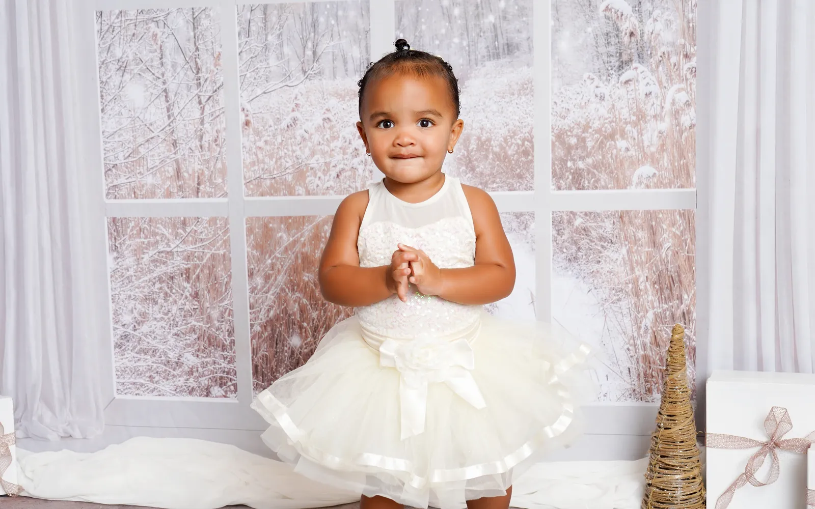 A toddler in a cream tutu standing in front of the snowy Winter Window