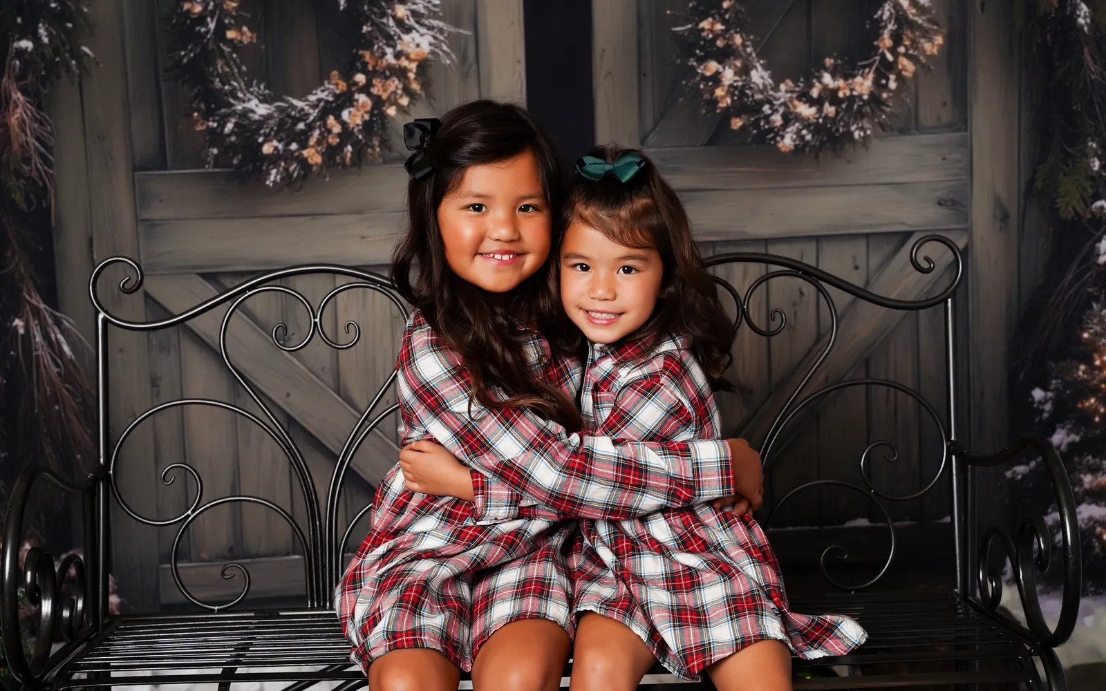 Two sisters in matching plaid hugging on a bench at the Cozy Christmas Barn