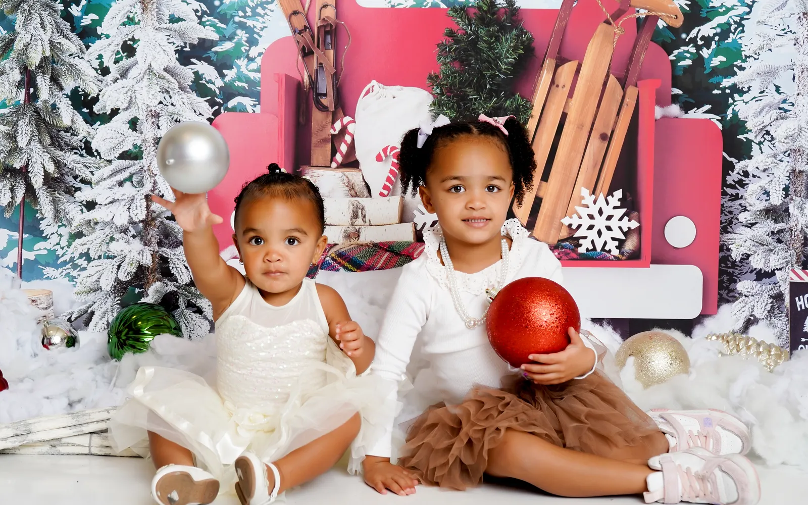 Two sisters holding ornaments in the snow in front of the Little Red Truck