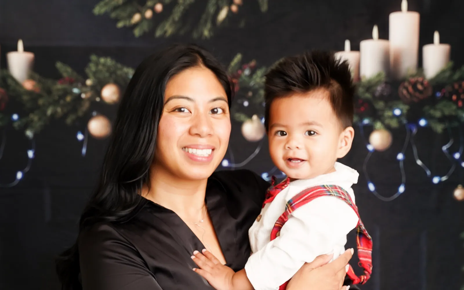 A mom holding her smiling baby on the candlelit Christmas Fireside set