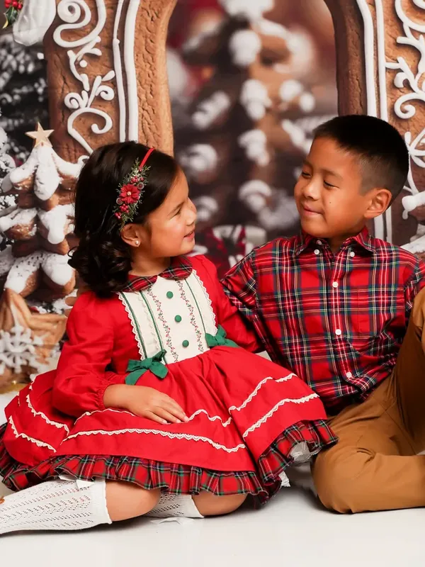 A brother and sister in red plaid smiling at each other on the Gingerbread Lane set at LaLa Holiday HQ