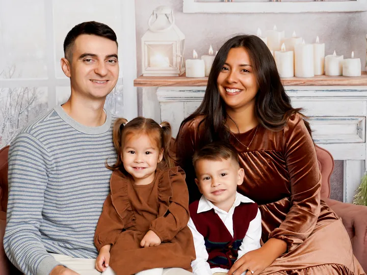 A family of four on the pink settee of the Sugarplum Christmas set at a Holiday HQ deluxe session