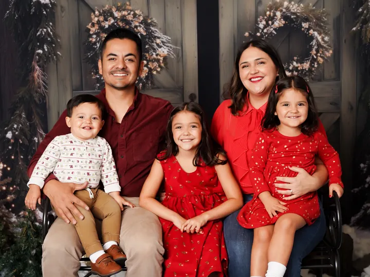 A family of five on a bench in front of the Cozy Christmas Barn doors at a Holiday HQ large family session