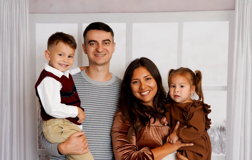 A family of four in front of the snowy Winter Window, with sheer curtains and a frosted meadow behind them